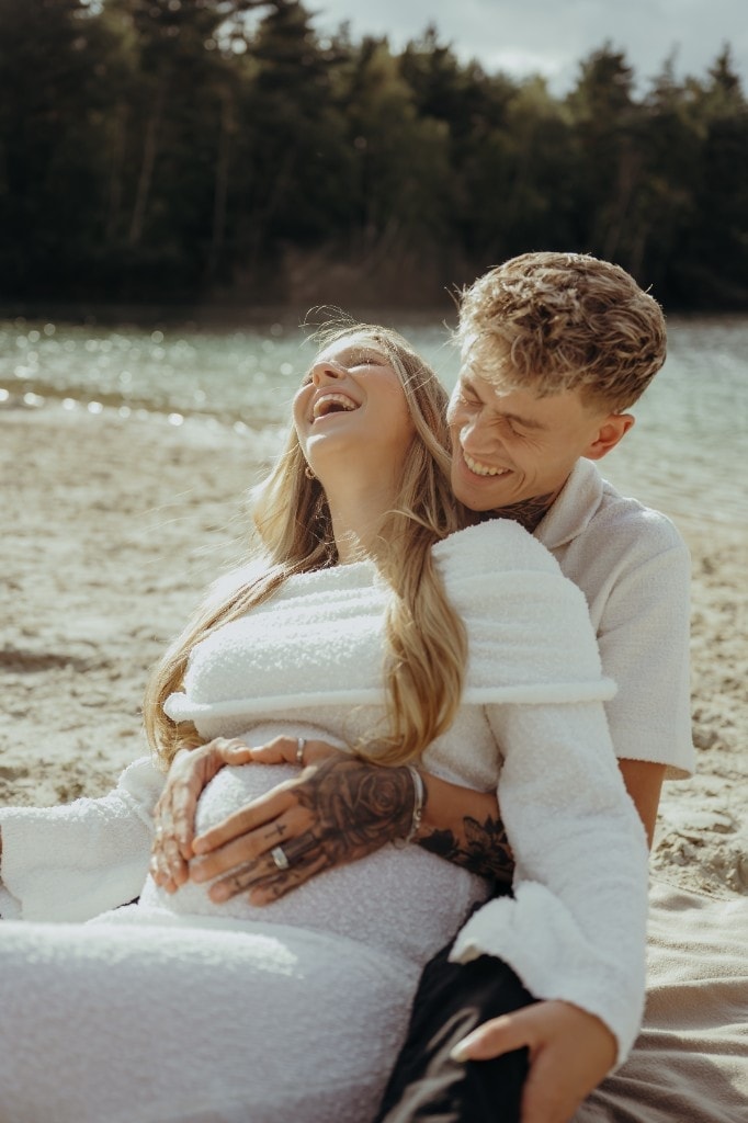 Babybauchshooting am See mit lachendem Paar