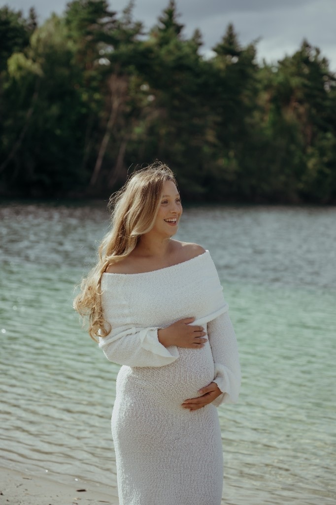 Schwangere Frau steht lachend am Wasser