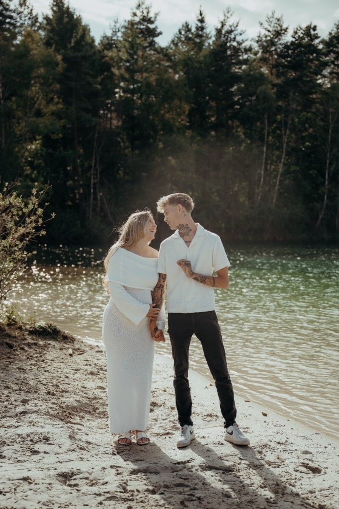 Paar lacht beim Babybauchshooting am See
