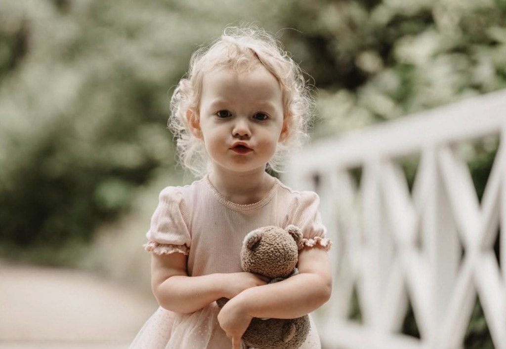 Kind mit Teddybär vor weißem Gartenzaun