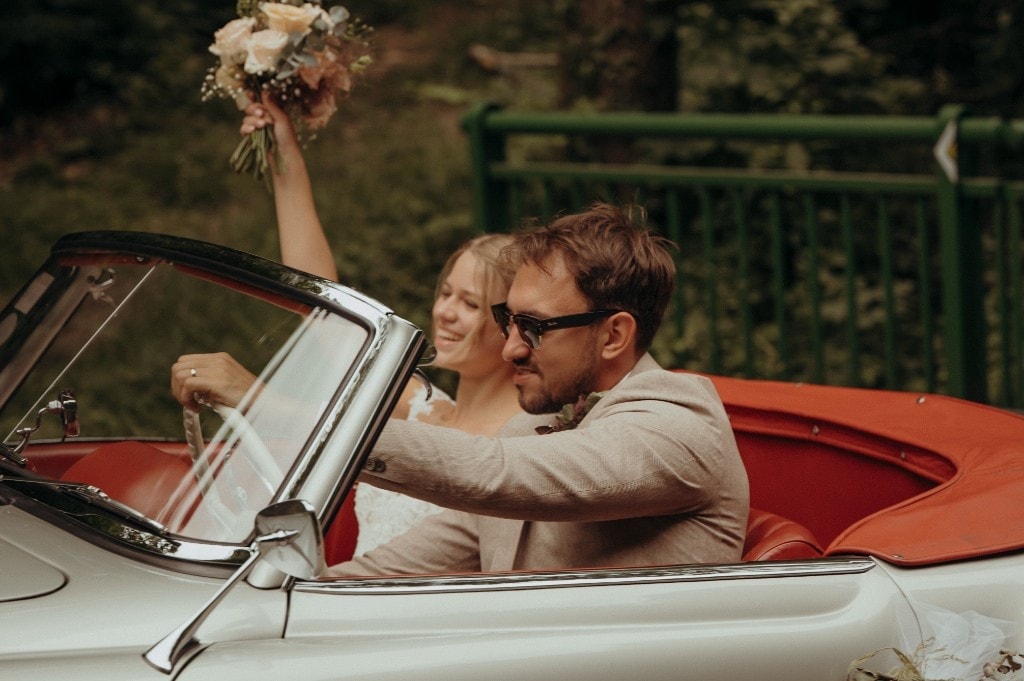 Brautpaar fährt lachend im Cabrio