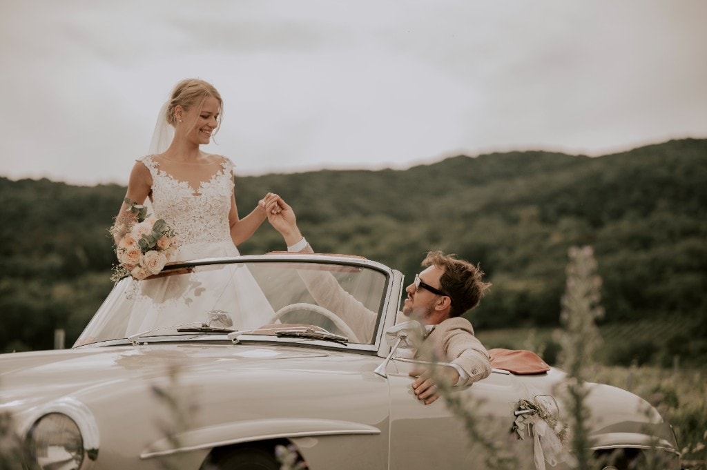 Braut auf dem Oldtimer in weiter Landschaft