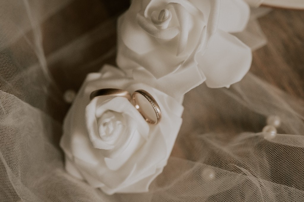 Trauringe auf weißen Rosen und Schleier