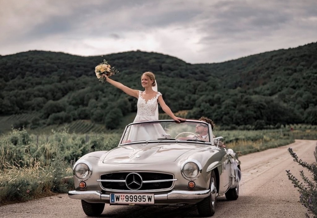 Braut mit Blumenstrauß im Cabrio, Bräutigam am Steuer
