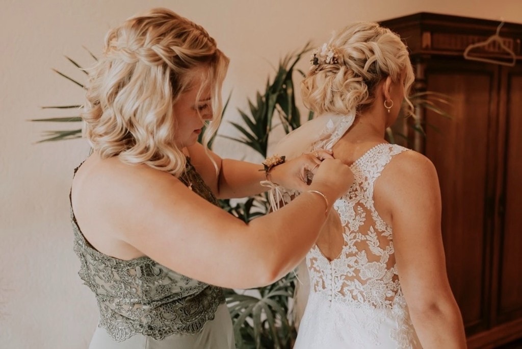 Getting Ready: Brautjungfer hilft der Braut in das Hochzeitskleid